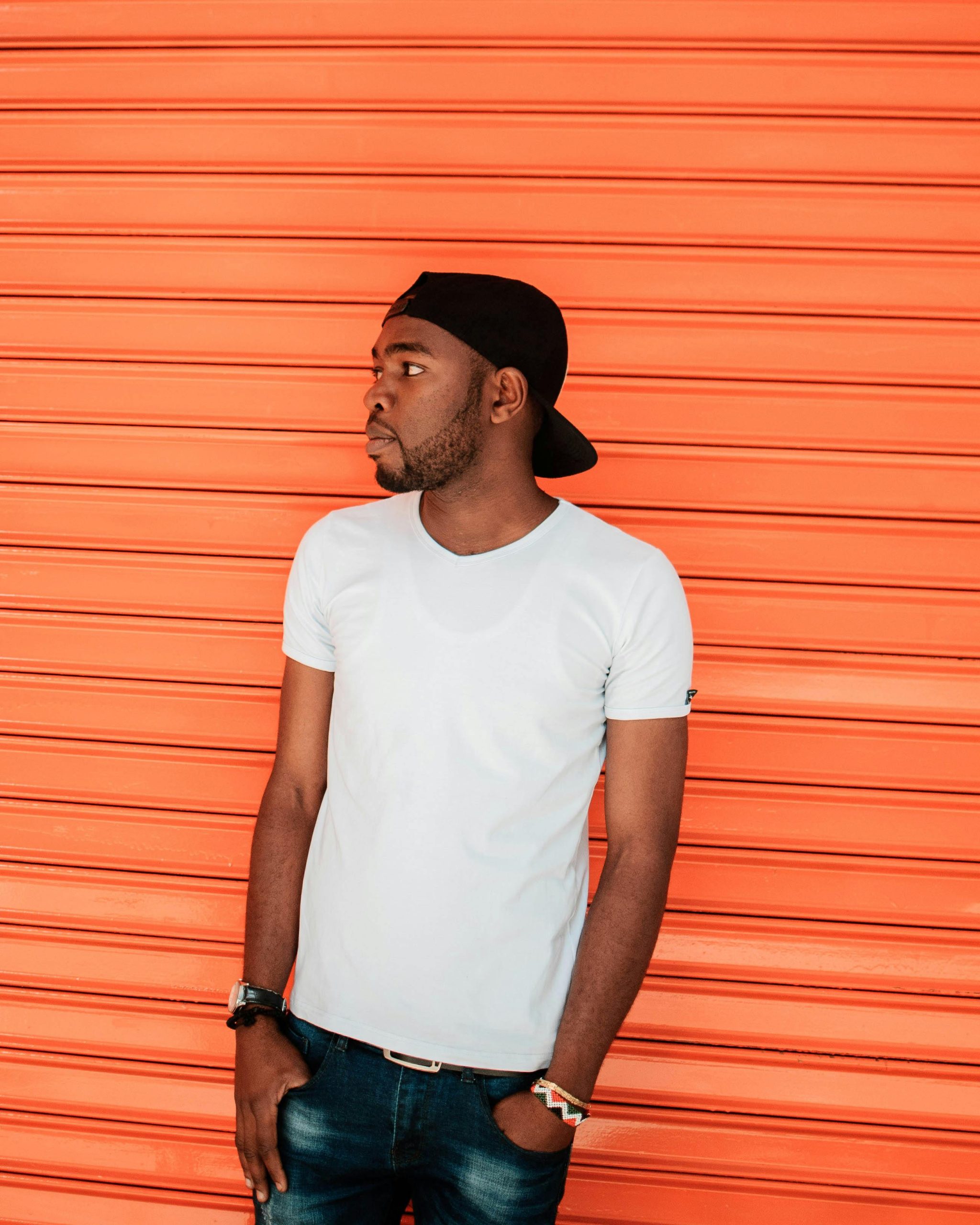 Side profile of a casual young man in a cap against an orange shutter in Nairobi.